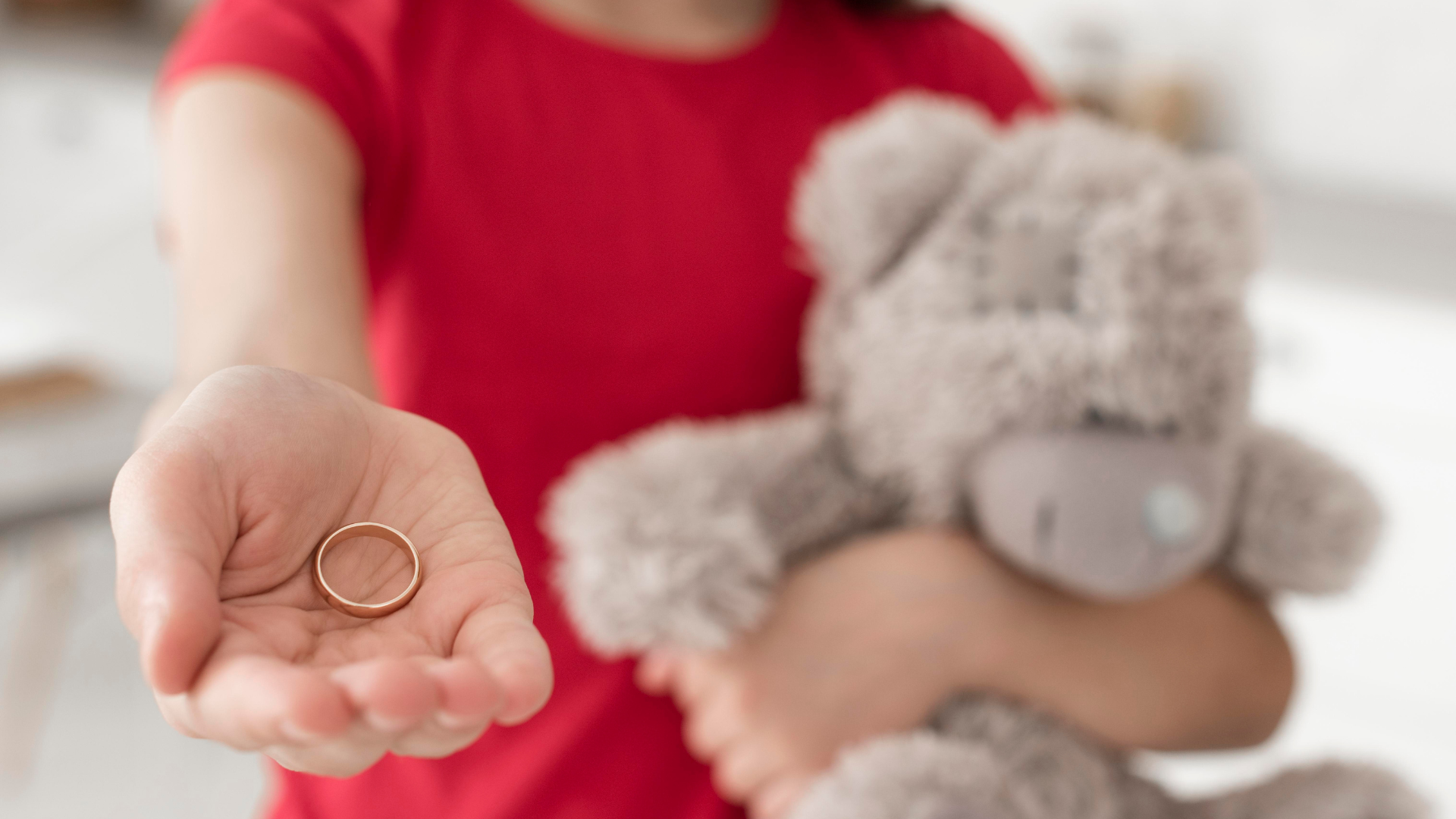 divorț cu copii implicați, adolescent care ține o mână întinsă cu o verighetă în ea și un ursuleț în cealaltă mână
